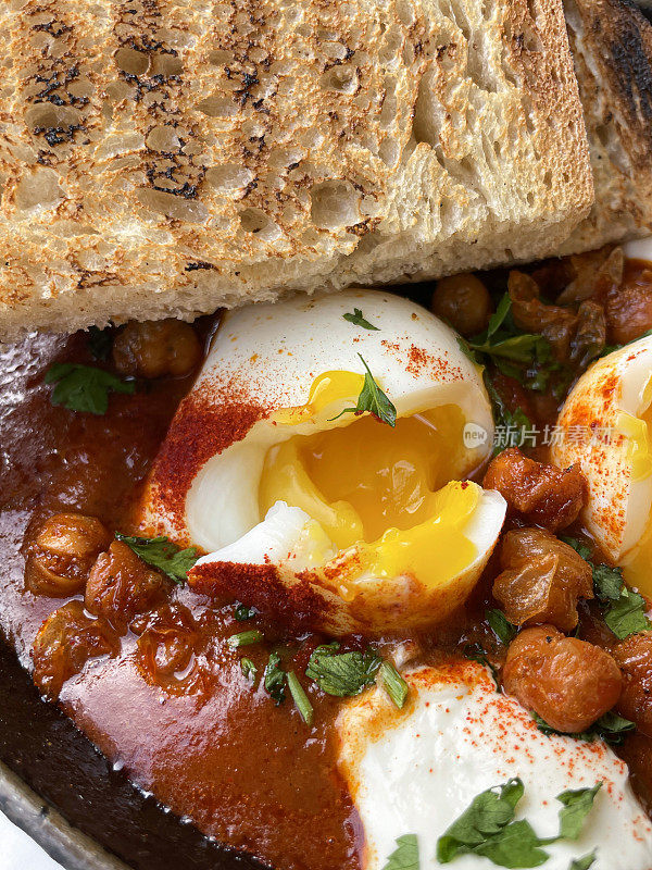 一锅地中海健康早餐的全画幅图片:shakshouka / shakshuka / chakchouka与烤面包片，鹰嘴豆，鸡蛋在番茄酱，辣椒，洋葱，橄榄油和大蒜中水煮，顶部有香菜，高架视图